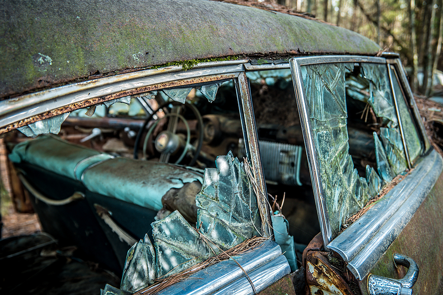 Old decaying car showing broken glass windows and rotting interior that is abandoned at a salvage yard.